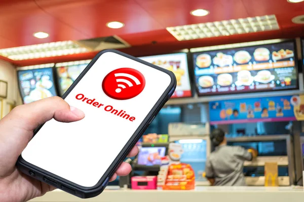 Order Foods Online on Mobile App, Application for food order on hand and abstract blur background in front of the fast food shop, office popular foods trend