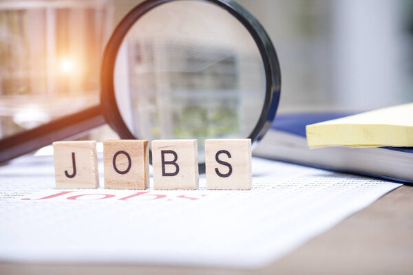 Концепция поиска вакансий, Большое красное текстовое слово "Работа" на белой бумаге и увеличительное стекло для поиска работы
