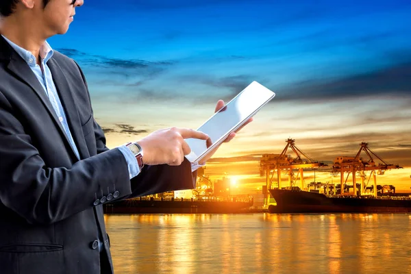 Businessman using digital tablet checking scheduled ship logistics and transportation of container Cargo port with working logistic import and export industry.