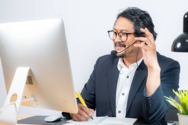 Orta yaşlı bir işadamı ciddi bir online toplantıda masasında oturuyor. Uzaktan çalışma, kurumsal stres, dijital iletişim ve iş sorunları kavramı..