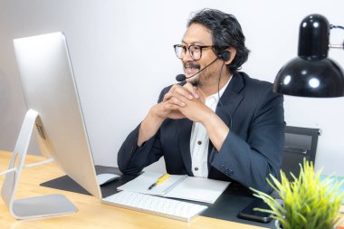 Orta yaşlı bir işadamı ciddi bir online toplantıda masasında oturuyor. Uzaktan çalışma, kurumsal stres, dijital iletişim ve iş sorunları kavramı..