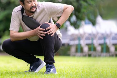 A young man holding his painful knee after running, concept of sports injury, exercise risk, and health care.