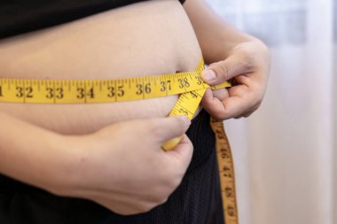 Asian woman using a tape measure around her waist to check body size and monitor health