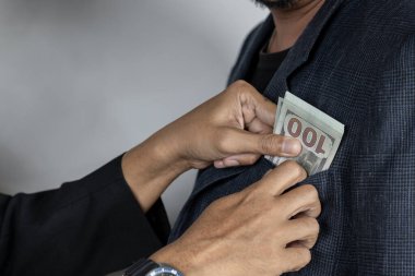 An illicit transaction taking place between two business professionals. One man is discreetly slipping a wad of cash into the inner pocket of another person's suit, symbolizing bribery and unethical business practices.