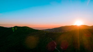 Gün batımının manzarası. Güneş, ışığa karşı görünen dağların ardında gizlenmek üzere. Ve arka planda deniz hafifçe görülür.