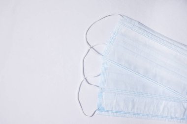 Resmin sağ tarafına beyaz bir zemin üzerine yerleştirilmiş üç beyaz yüz maskesi..