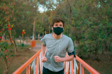 Yüz maskeli genç bir adam parkta spor kıyafetleriyle egzersiz yapıyor..