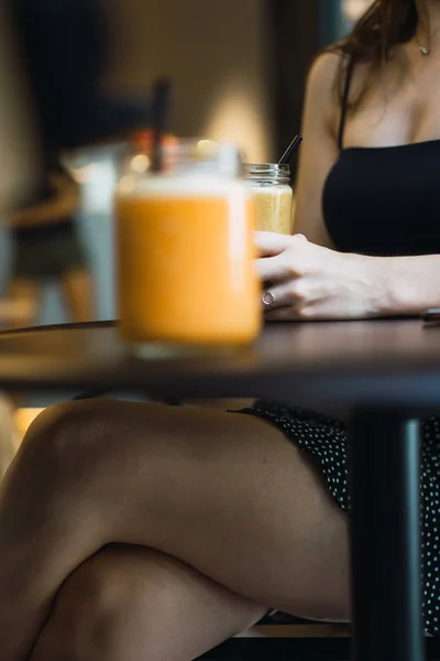 Ürün Görünümü parlak lezzetli içecek ile karanlık masada oturan siyah elbiseli Genç kadının çıplak çapraz bacak arka plan bulanık
