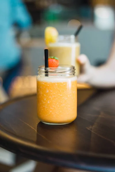 Kokteyl kavanoza bulanık arka plan üzerinde koyu yuvarlak ahşap masa yerleştirilen çilek ile dekore parlak turuncu tastydrink görünümünü kapat