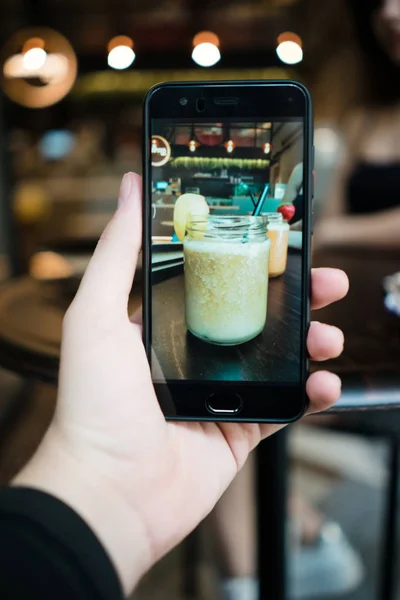 Cep telefonu ve içki alarak resmi ekranda karanlık kafe tablonun arka plan bulanık kokteyl kavanoza tutan el görünümünü kırpma