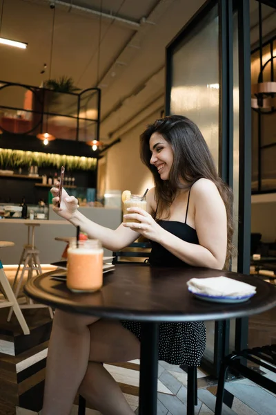 Attractivebrunette erkek ahşap masa başında oturan ve saç dokunmadan kameraya bakarak omuz üst kapalı beyaz yaz aylarında yan görünüm