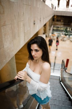 Yürüyen merdiven gidiyor ve uzakta bulanık arka plan üzerinde seyir çıplak omuz ile beyaz yaz en güzel genç esmer kadın 