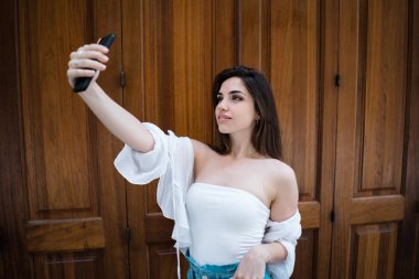 Attractivebrunette erkek ahşap masa başında oturan ve saç dokunmadan kameraya bakarak omuz üst kapalı beyaz yaz aylarında yan görünüm