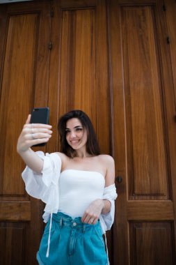 Attractivebrunette erkek ahşap masa başında oturan ve saç dokunmadan kameraya bakarak omuz üst kapalı beyaz yaz aylarında yan görünüm