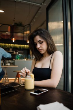 Çekici genç esmer kadın koyu ahşap kafeterya masada siyah en iyi oturma ve bulanık arka plan üzerinde kokteyl kavanoza içki karıştırma rahat