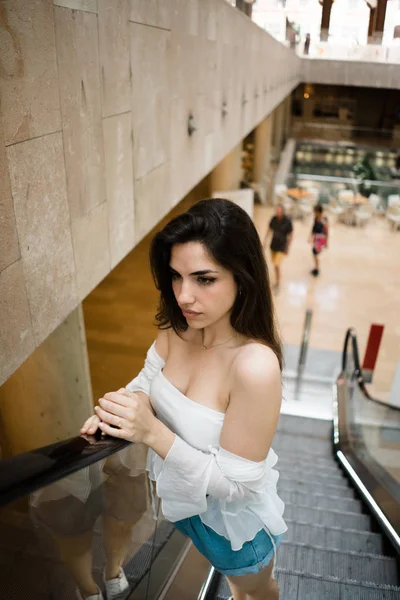 Yürüyen merdiven gidiyor ve uzakta bulanık arka plan üzerinde seyir çıplak omuz ile beyaz yaz en güzel genç esmer kadın 