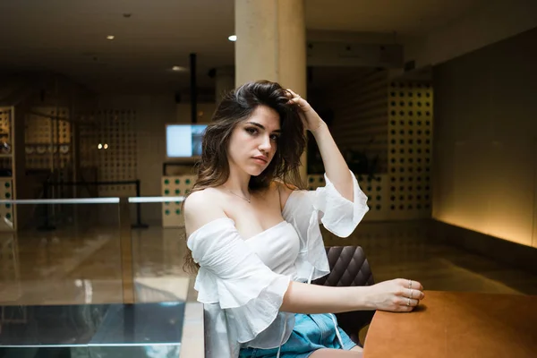 Attractivebrunette erkek ahşap masa başında oturan ve saç dokunmadan kameraya bakarak omuz üst kapalı beyaz yaz aylarında yan görünüm