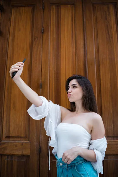 Attractivebrunette erkek ahşap masa başında oturan ve saç dokunmadan kameraya bakarak omuz üst kapalı beyaz yaz aylarında yan görünüm