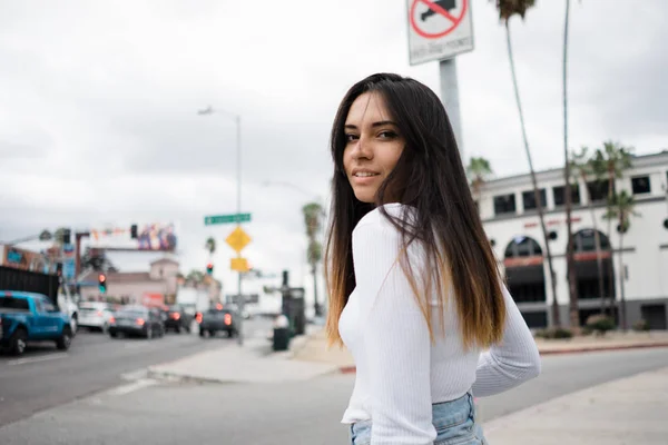 Gülümseyen ve kamera modern şehir sokakta road yakınındaki dururken bakarak gündelik kıyafet içinde çekici genç kadın yan görünüm
