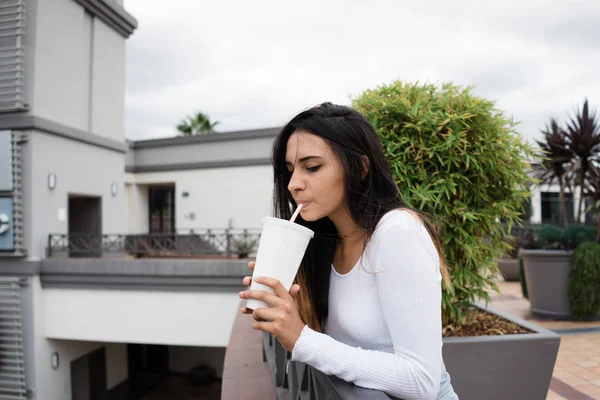 Bulutlu gün modern binanın terasında güzel genç esmer zevk lezzetli içecek dururken yan görünüm
