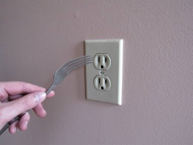 Duvardaki bir elektrik prizine çatal takan biri.