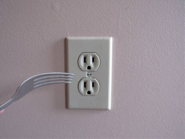 Duvardaki bir elektrik prizine çatal takan biri.