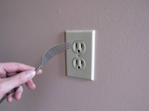 插叉的人把叉子插进墙上的电源插座的人 — 图库照片