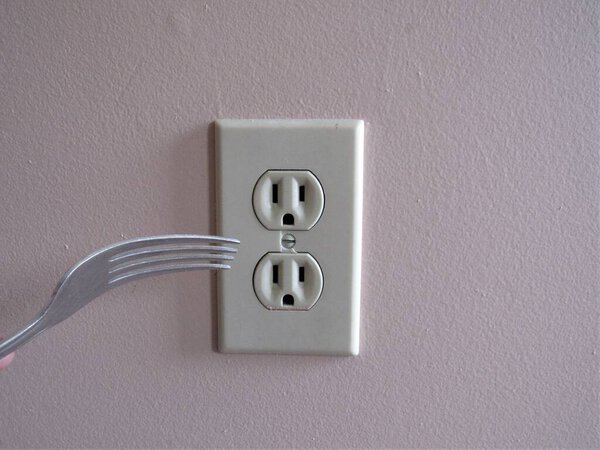 A person putting a fork into an electrical outlet on the wall