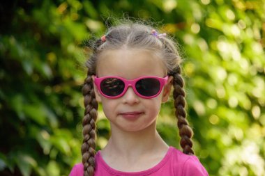 Yeşil arka planda güneş gözlüklü küçük beyaz kız portresi