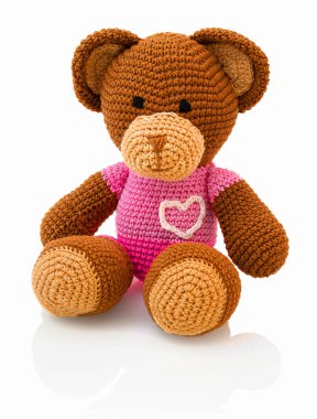 Beyaz arka planda izole edilmiş, gölge yansıması olan şirin bir tığ işi ayı bebeği. Oyuncak örülü oyuncak ayı beyaz altında oturuyor. Doldurulmuş peluş oyuncak ayı..