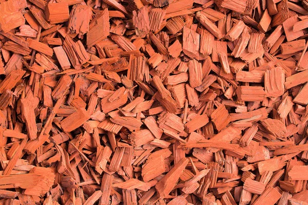 Red wood chips. Natural texture background of red wooden pieces of tree bark. Wood chips, mulch for gardening or natural themes. Full filled frame picture. Landscaping red colored materials.Above view