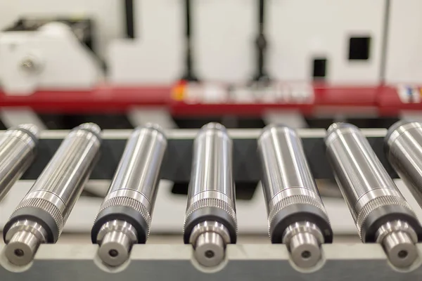 Lined up magnetic cylinders for die cut on rotary printing press. Magnetic cylinder for flexo rotary die cutting. Magnetic roll and in-line press machine in background. Cylinder for cutting dies.