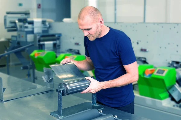 Flexo döner kalıp kesme hazırlık. Silindirik kalıp hazırlama baskı makinesi yanında duran yazdırma fabrika işçisi. Operatör manyetik rulo kesme ölmeye hizalar. Etiket imalat.