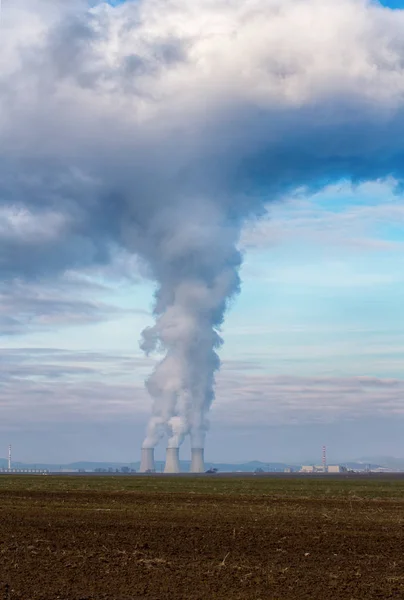 Cooling towers of nuclear power plant (NPP) Jaslovske Bohunice (EBO) in Slovakia. Clouds of thick smoke from chimneys on blue sky at winter day. Cooling towers of power plant with water steam.