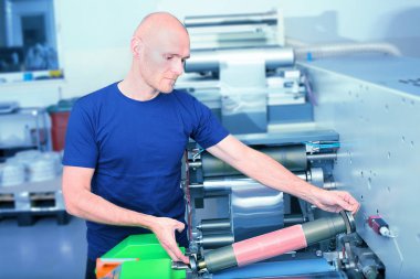 Polimer kabartma tabak ile baskı silindir tutan yazıcı operatör baskı makinesi yanında üzerinde sıkışmış. Yazdırma işlemi için hazırlık hatlı basın makine üzerinde gösterilen sahne.