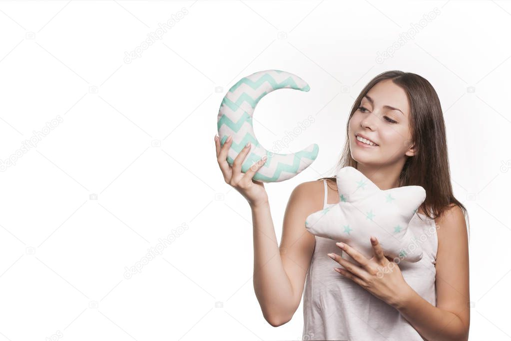 Beautiful young brunette on a white background holding a pillow in the shape of a star and moon