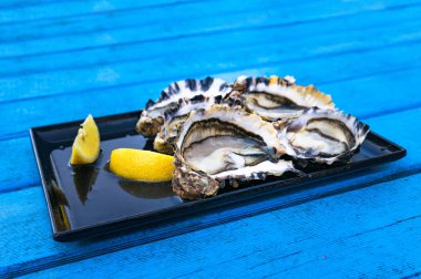 Açık havada açık yemek, parlak mavi ahşap masa üzerinde limonlu taze çiğ istiridye