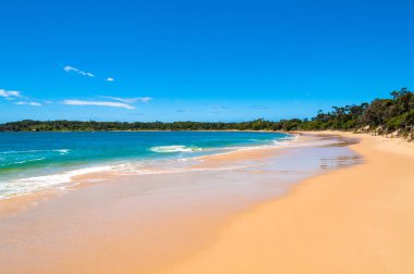 Yumuşak dalgalar ve mavi gökyüzü ile pitoresk kum plaj
