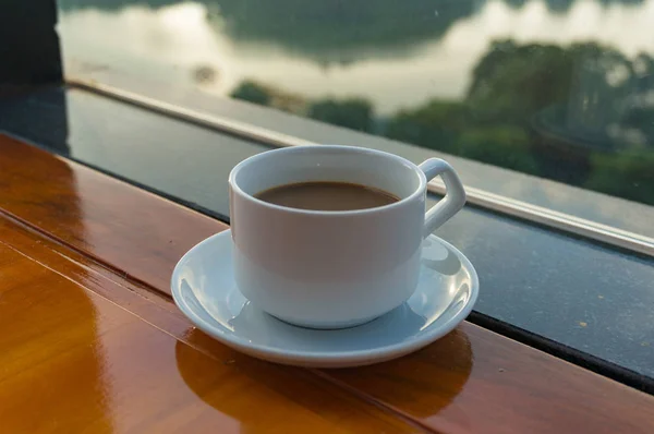 Filiżanka kawy na stole w kawiarni z widokiem na wodę — Zdjęcie stockowe