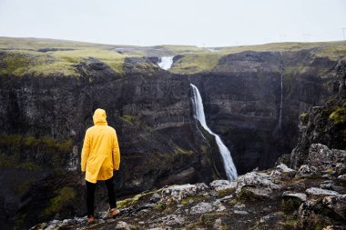 İzlanda'daki şelale Haifoss. Genç bir adam bir uçurumun üzerinde duruyor ve şelale görünüyor. 