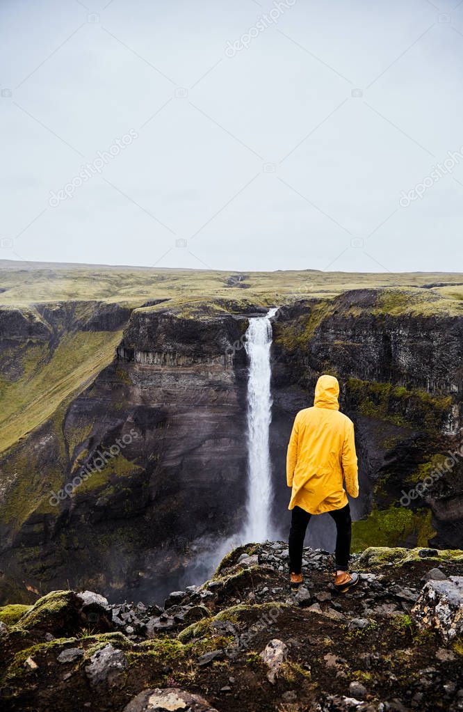 Waterfall Haifoss in Iceland. A young guy stands on a cliff and looks at the waterfall. 