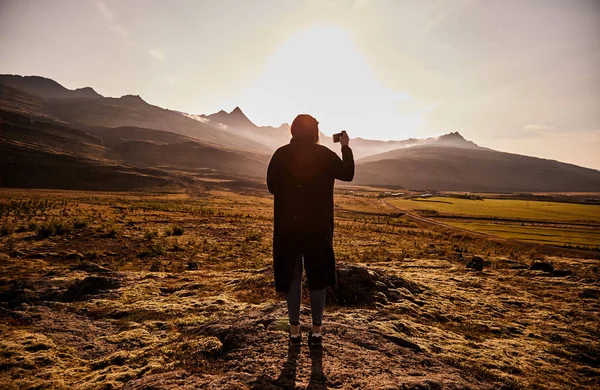 Sylwetka młoda dziewczyna, która robi zdjęcia w telefonie islandzkiego krajobrazu. Zachód słońca w Islandii. — Zdjęcie stockowe