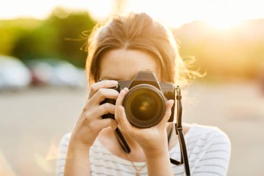 Günbatımında bir yaz parkta fotoğraf makinesinde resimleri alarak genç kız