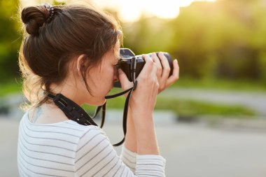 Günbatımında bir yaz parkta fotoğraf makinesinde resimleri alarak genç kız