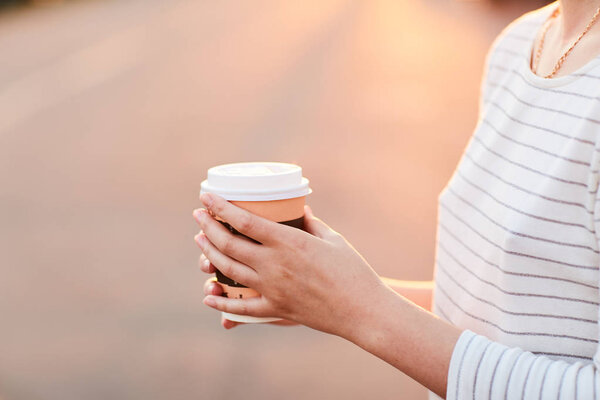 young girl holding paper Cup with hot coffee at sunset