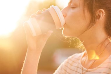 Genç kadın günbatımında kağıt bardak kahve içme