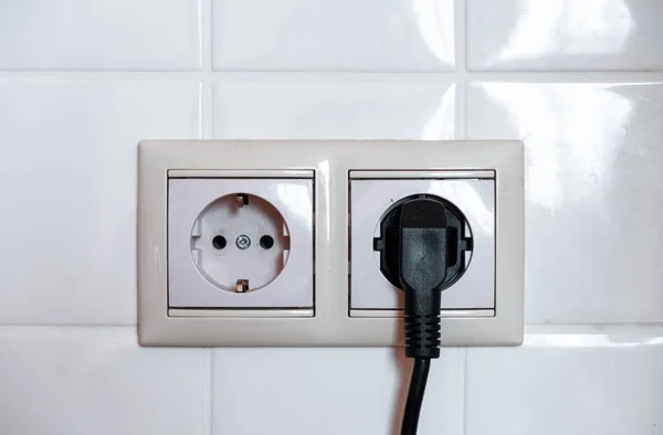 Enchufe eléctrico negro. Dos zócalos sobre un fondo de baldosas blancas . — Foto de Stock