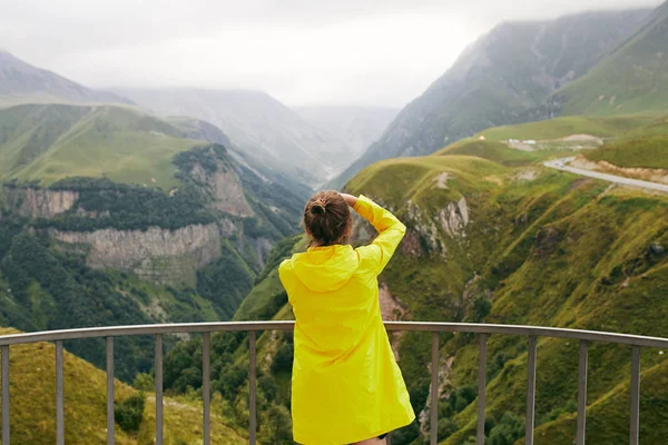 Egy fiatal lány, egy sárga esőkabátot fényképek a hegyekben. Grúzia. Nyári. Augusztus. Lány így egy fotózást a hegyi. — Stock Fotó