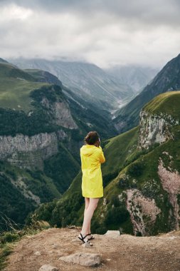 Genç bir kız sarı yağmurluk içinde dağlar fotoğraflar. Gürcistan. Yaz. Ağustos. Kız bir fotoğraf çekimi Dağı'nın yapım. 