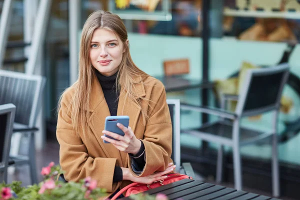 ロシア少女が携帯電話のメッセージを入力します。女の子は、Sms メッセージを書き込みます。ソーシャル ネットワークで通信します。市内中心部のカフェで座っている女性 — ストック写真